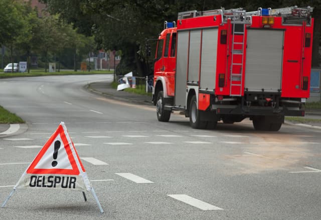 Feuerwehr-Einsatz mit Ölspur-Warndreieck auf der Fahrbahn